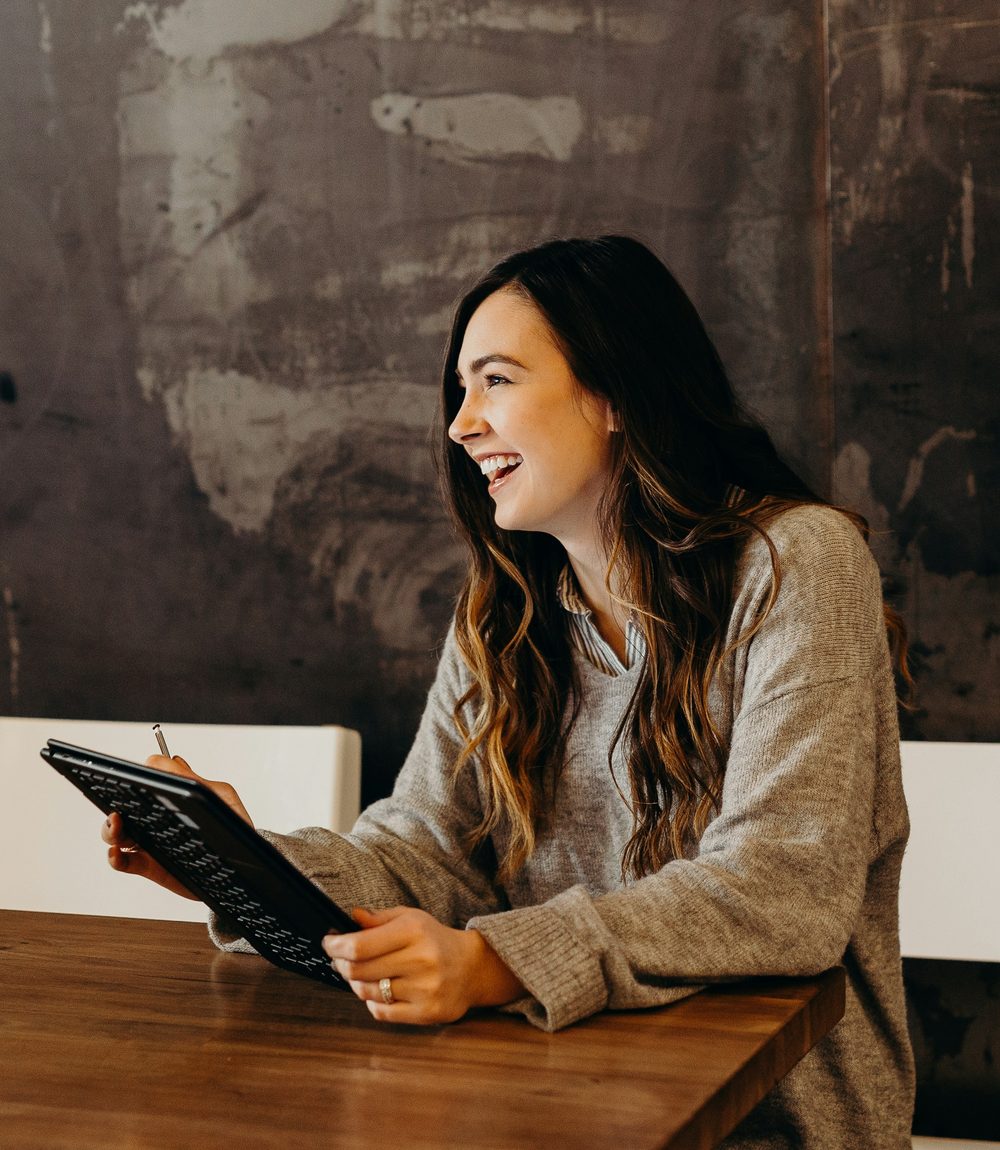 A business owner sitting at a table with a tablet, mid-conversation and laughing.